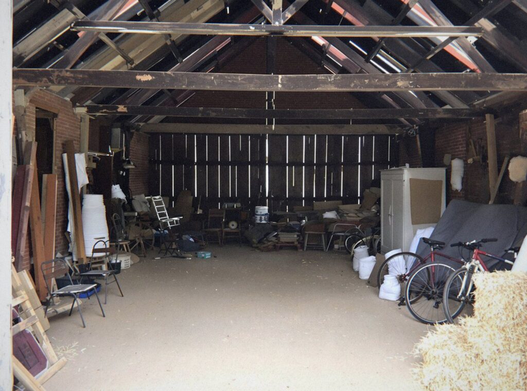 Grange en brique de l'Ain encombrée de planches, de vélos, de meubles et de bottes de paille avant son débarras