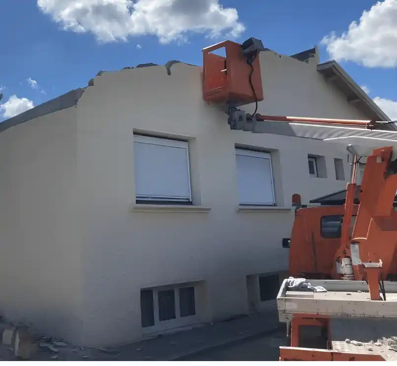Nacelle de MJ Démolition contre le pignon d'une maison pendant le démontage de sa toiture